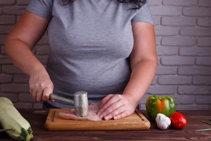 Overweight woman pounding chicken breast as part of LCHF diet