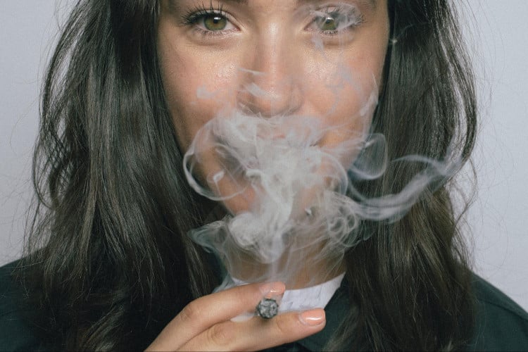 Dark haired woman blowing smoke from cigarette